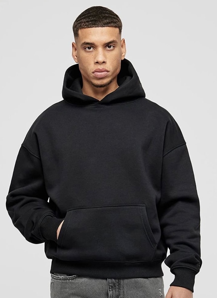 Man wearing a black hoodie standing confidently in a minimalist fashion pose.